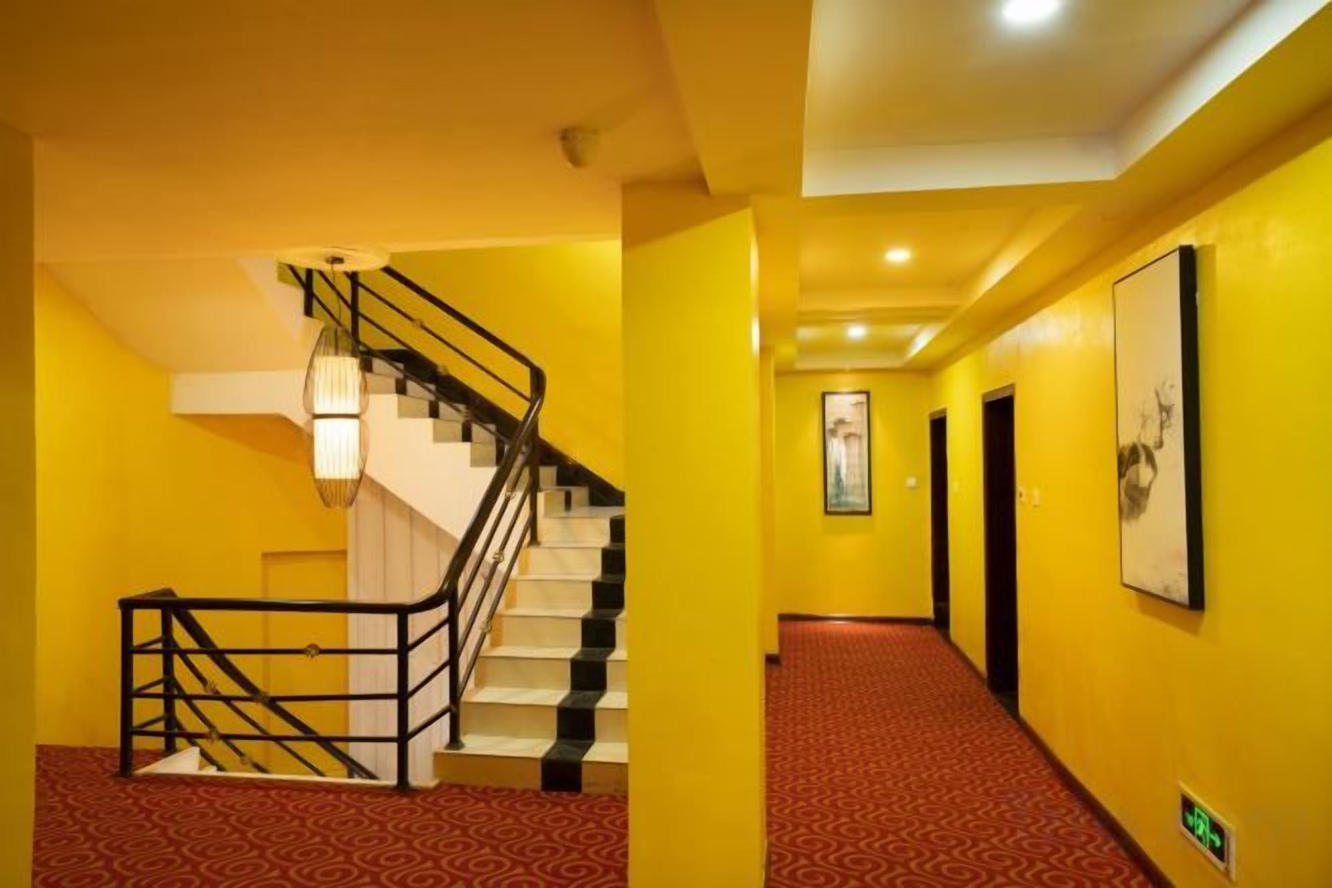 A hotel hallway with a staircase, red carpet, and framed artwork on the walls.