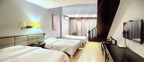 A hotel room with three beds, a desk, a TV, and a staircase.