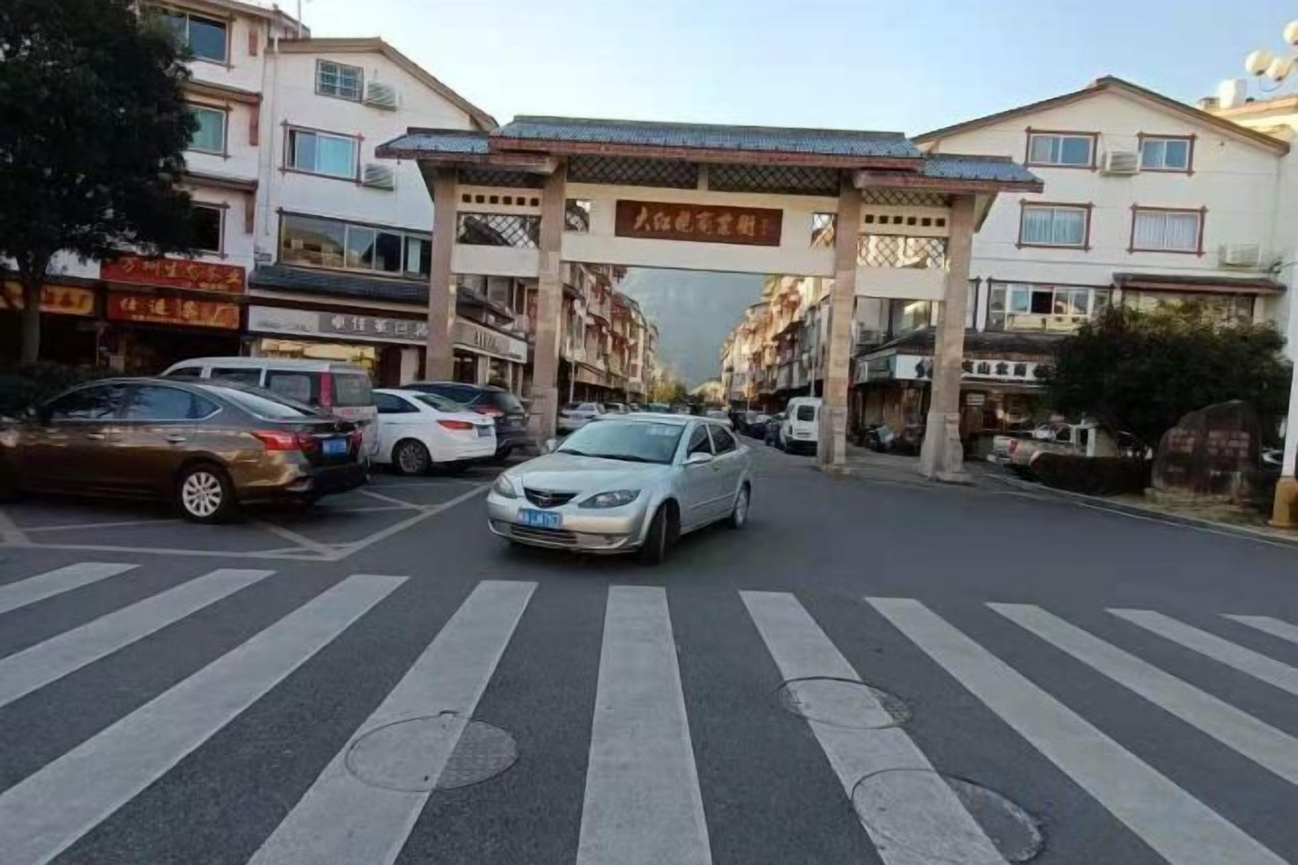 A street view with a pedestrian crossing, parked cars, and a building with a traditional entrance.