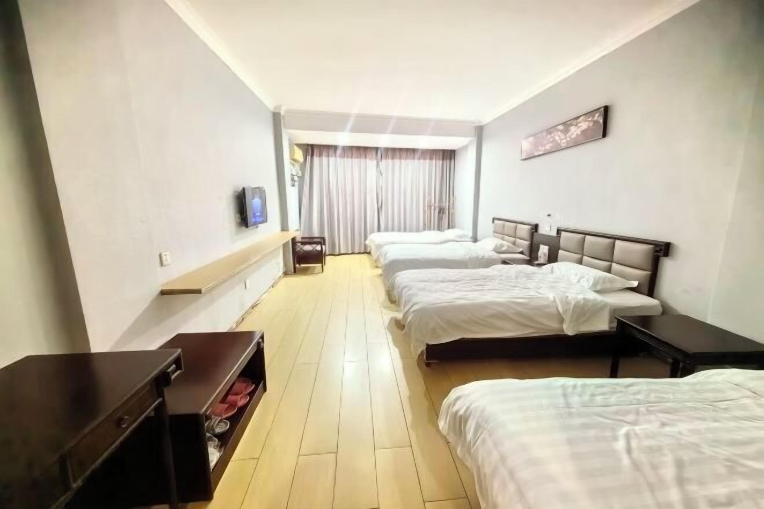 A hotel room with two beds, a desk, a TV, and a window with curtains.