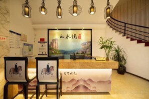 A reception area with a counter, framed artwork, chairs, and a staircase. - Wuyishan Shanshuiyue Hotel (Sangu Resort Area) (Wuyishan)