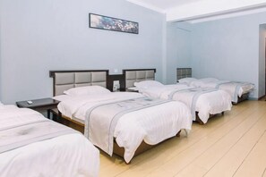Una habitación de hotel con cuatro camas individuales, una mesita de noche pequeña con lámpara, y un cuadro en la pared.