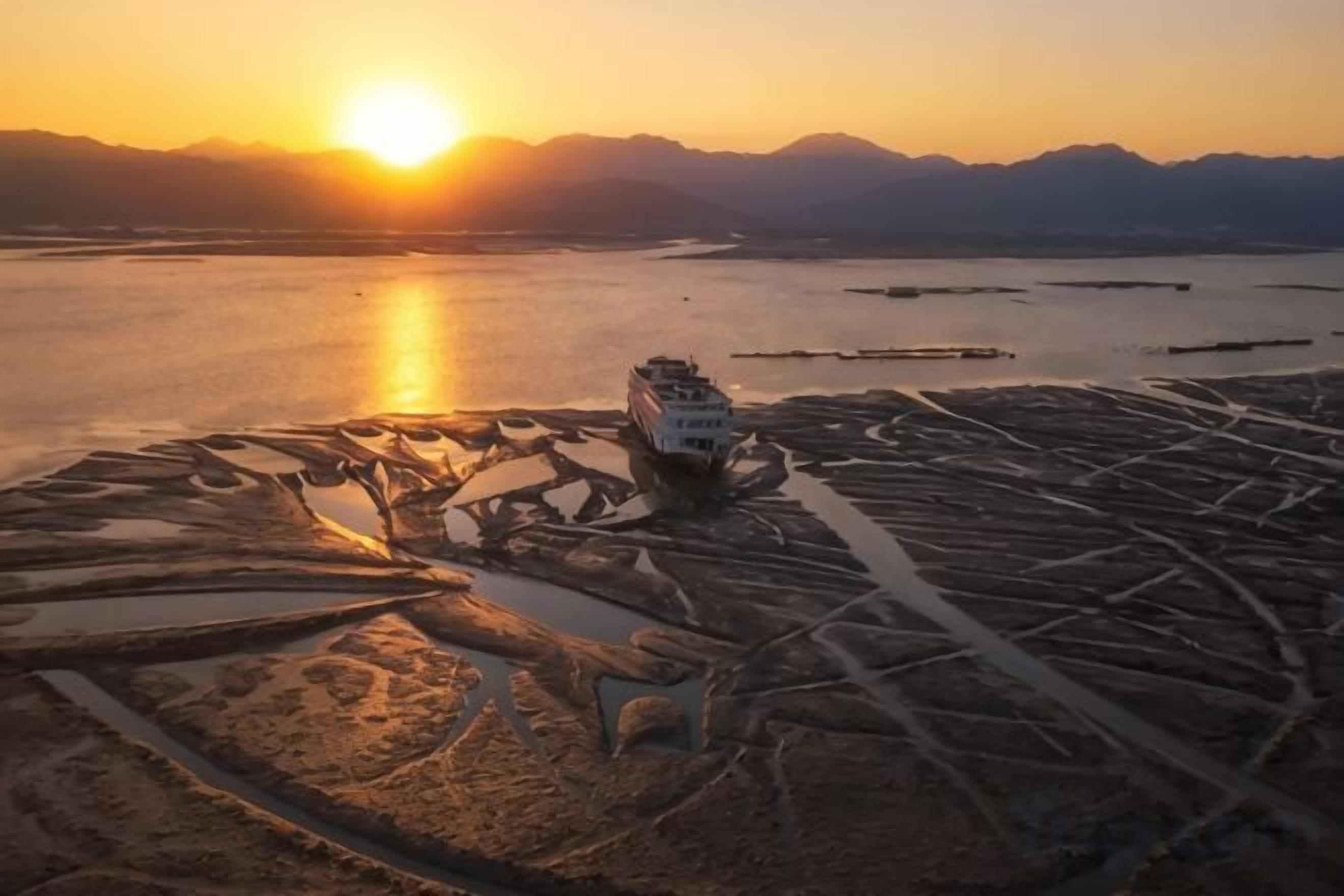 A ship on a dry riverbed with mountains in the background.