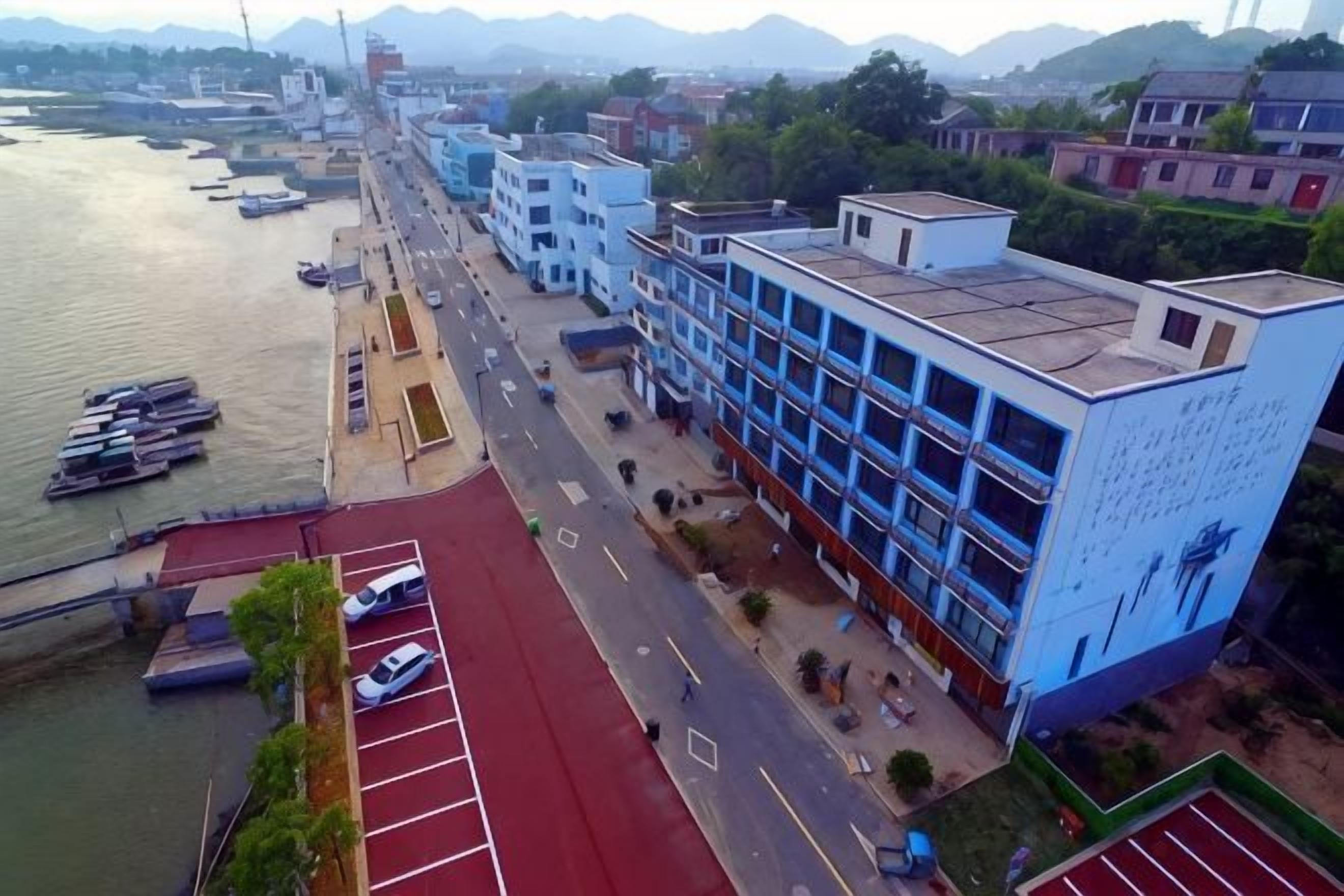 A riverside building with a red sports court, a parking area, and a blue facade with a mural.