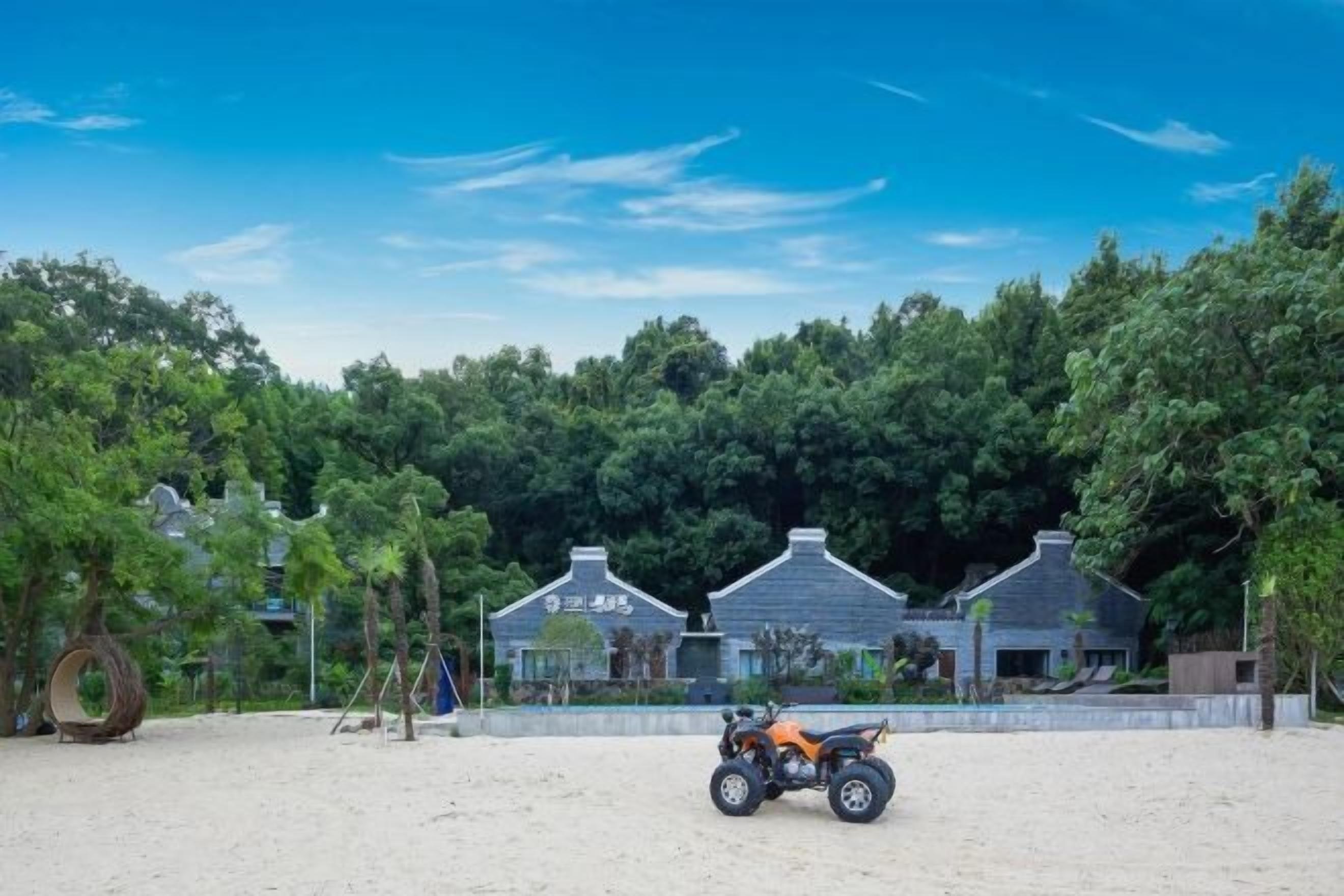 A sandy beach area with a small building and trees in the background.