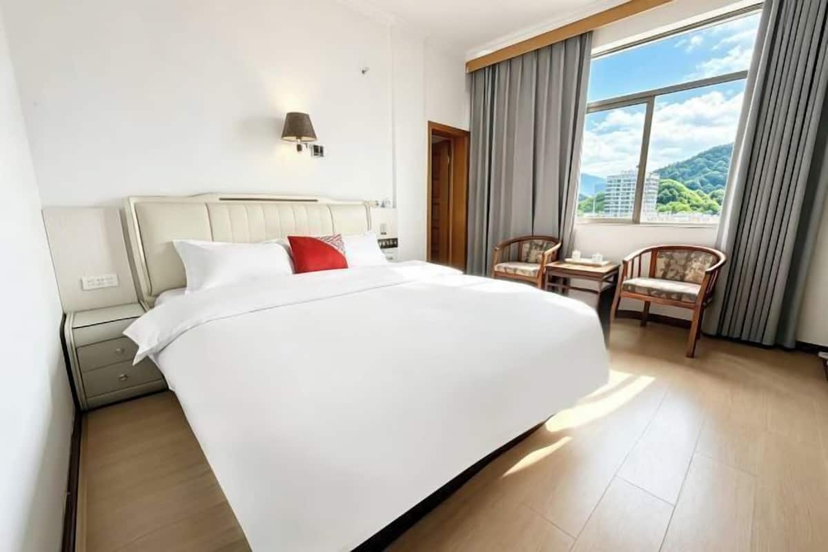 A hotel room with a large bed, a nightstand, a chair, a small table, and a window with curtains.