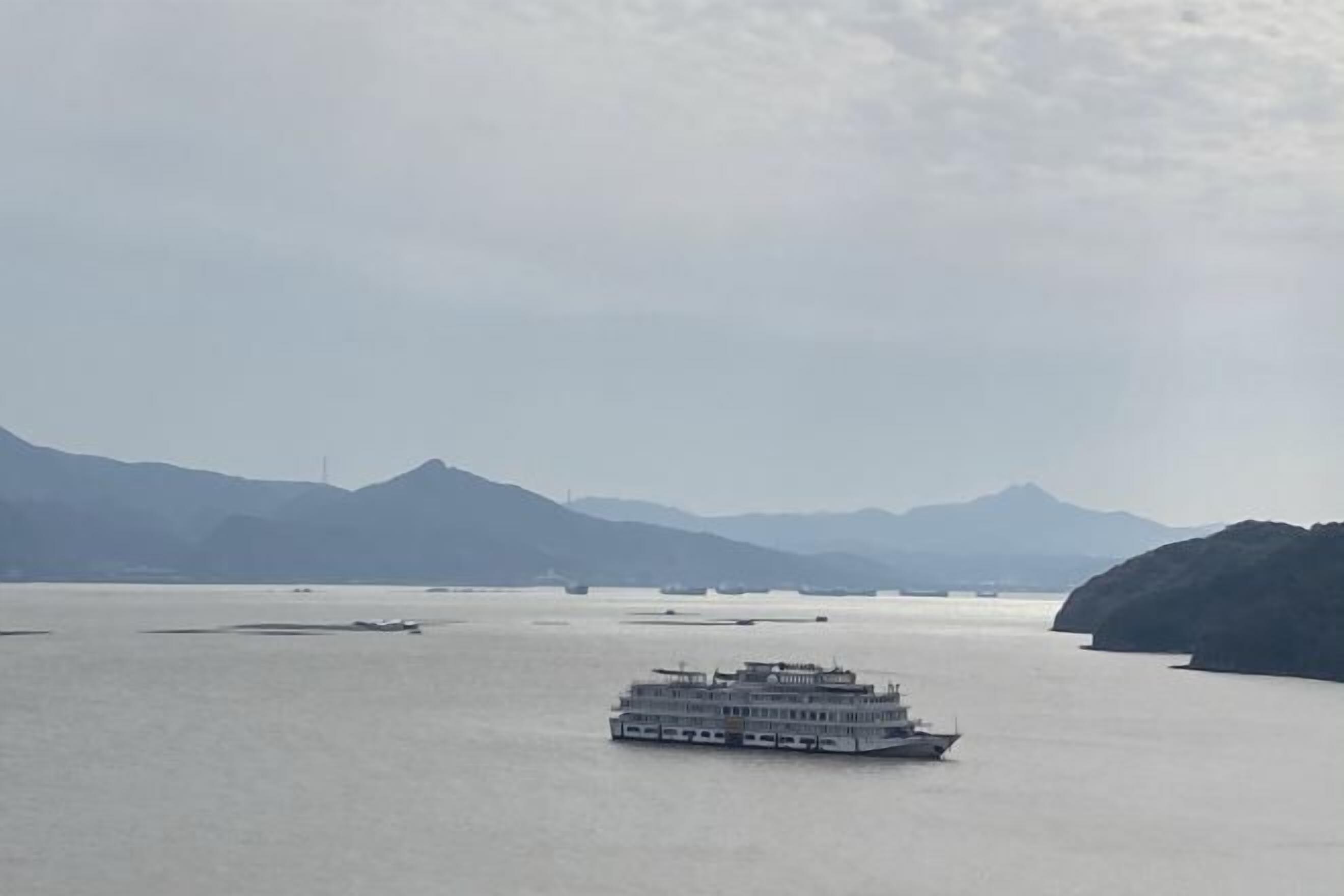 A large riverboat on calm water with mountains in the background.