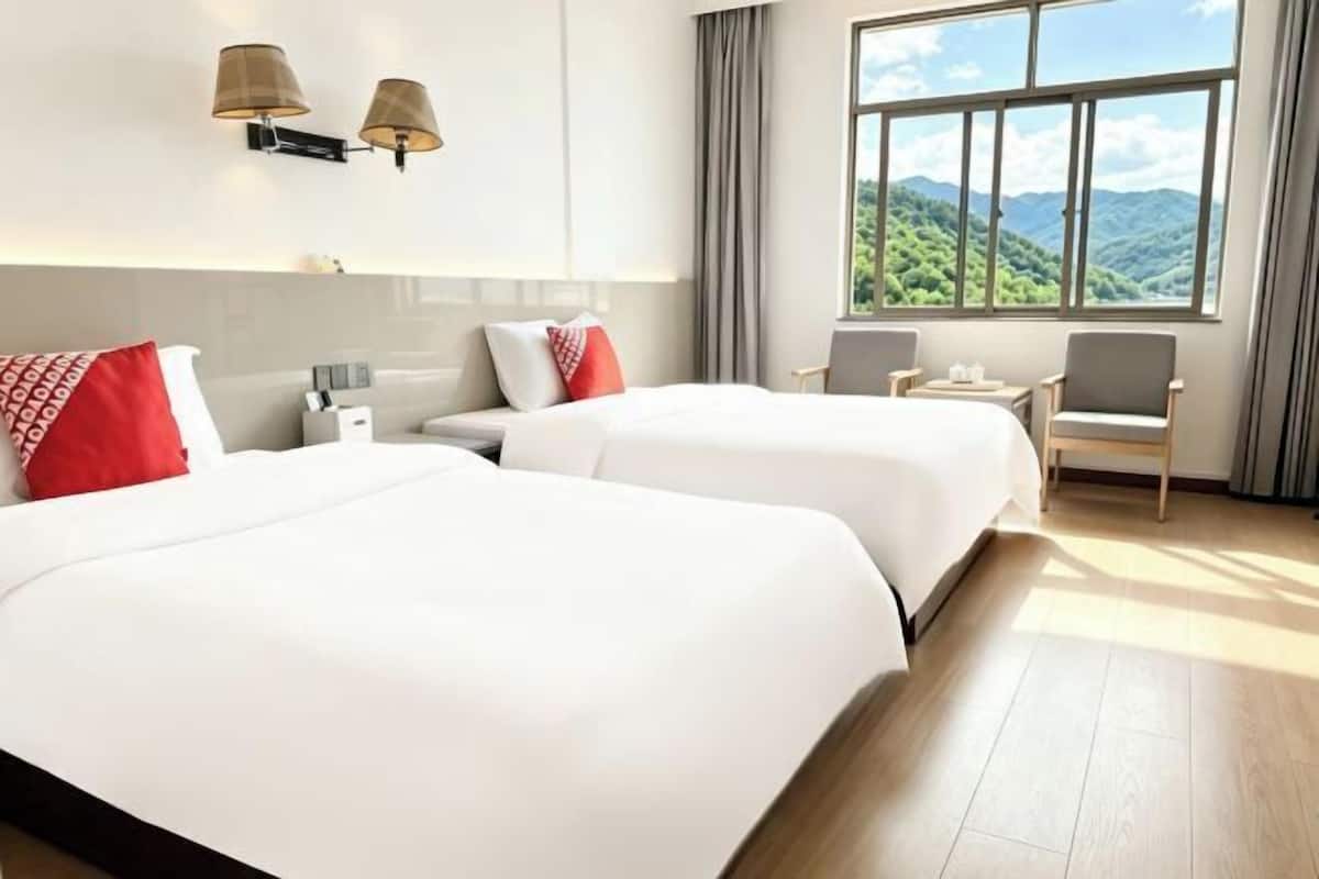 A hotel room with two beds, a chair, a desk, and a large window with a mountain view.