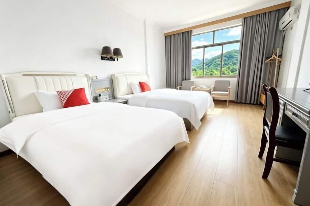 A hotel room with two beds, a desk, a chair, a small table, and a window with curtains.