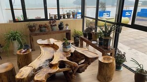 A wooden table with a unique design, surrounded by potted plants and wooden stools in a room with large windows. - Huanqiu Hotel (Ninghai)