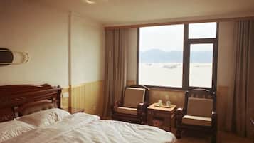 A hotel room with a large bed, two armchairs, a small table, and a window with a view of a body of water and mountains.