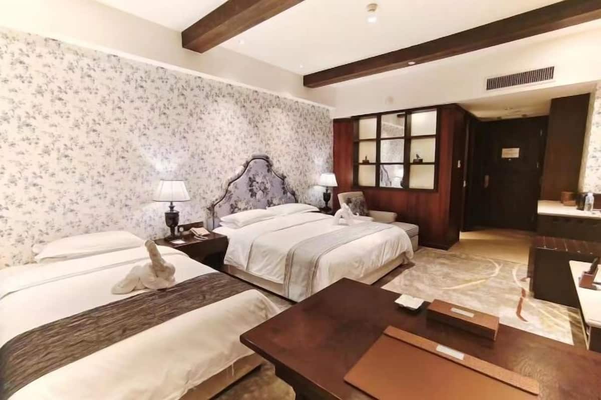 A hotel room with two beds, a wooden headboard, a desk, and a mirror.