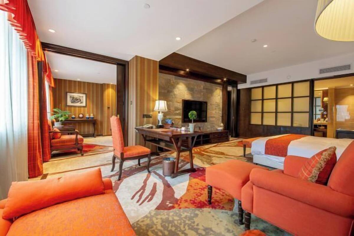 A hotel room with a sofa, a desk, a chair, a fireplace, and a television.
