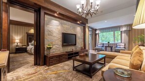 A hotel room with a stone accent wall, a flat-screen TV, a sofa, a coffee table, and a dining area. - Kunming Jiali Ze Saville Royal Hotel (Songming)