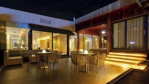 An outdoor seating area with tables and chairs, a wooden deck, and a staircase leading to an upper level. - Kunming Jiali Ze Saville Royal Hotel (Songming)