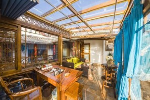A room with a wooden table, chairs, a sofa, and a large window with curtains. - Lijiang Clouds flying high Inn (Lijiang)
