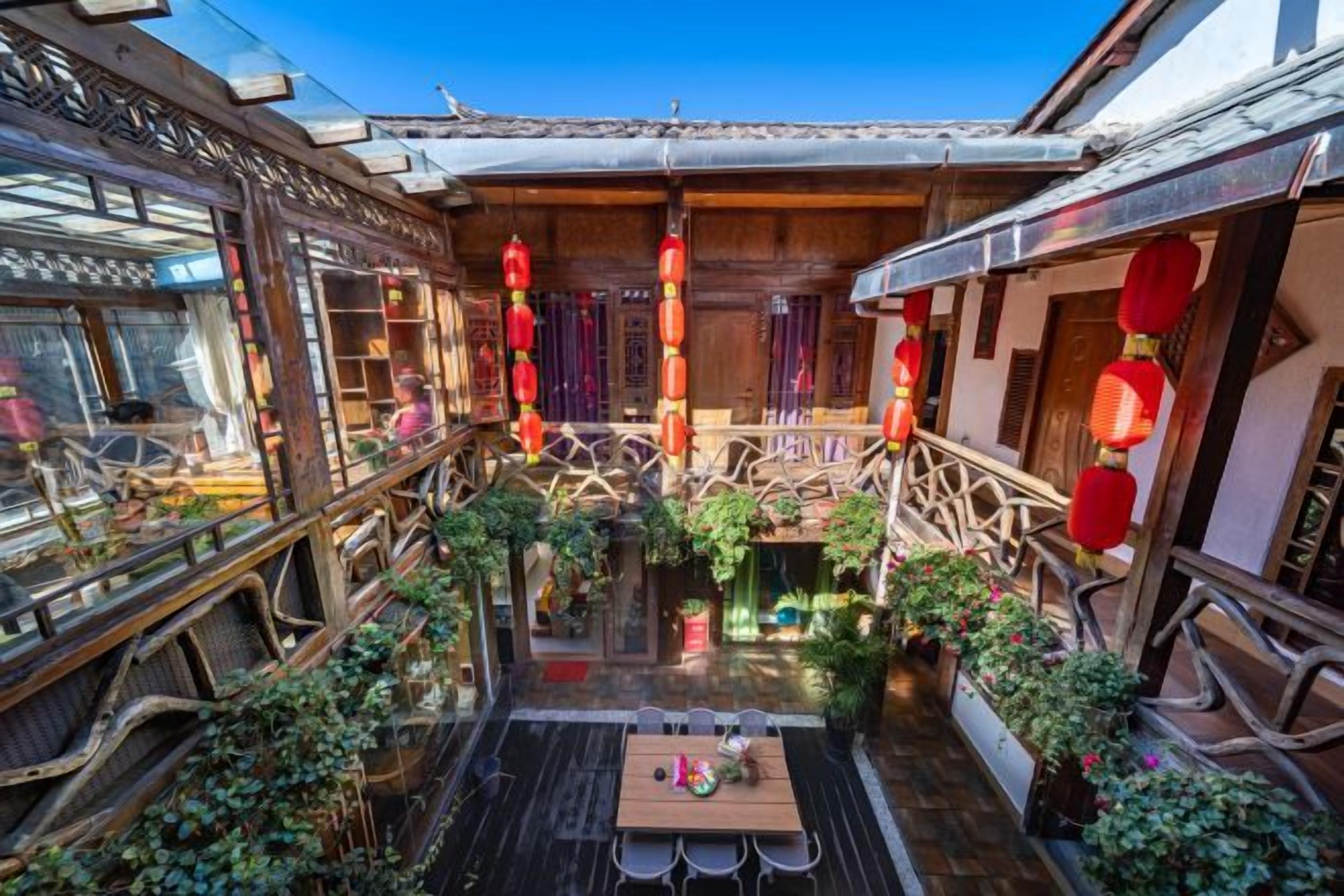 A traditional courtyard with a wooden table, potted plants, and red lanterns.