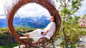 A person sitting in a circular wicker chair with a view of a mountainous landscape. - Lijiang Clouds flying high Inn (Lijiang)