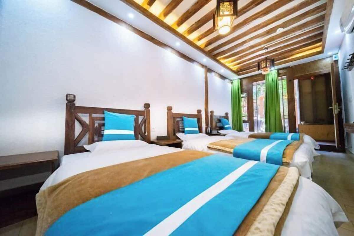 A hotel room with wooden beams, multiple beds with blue and white bedding, and a green curtain.