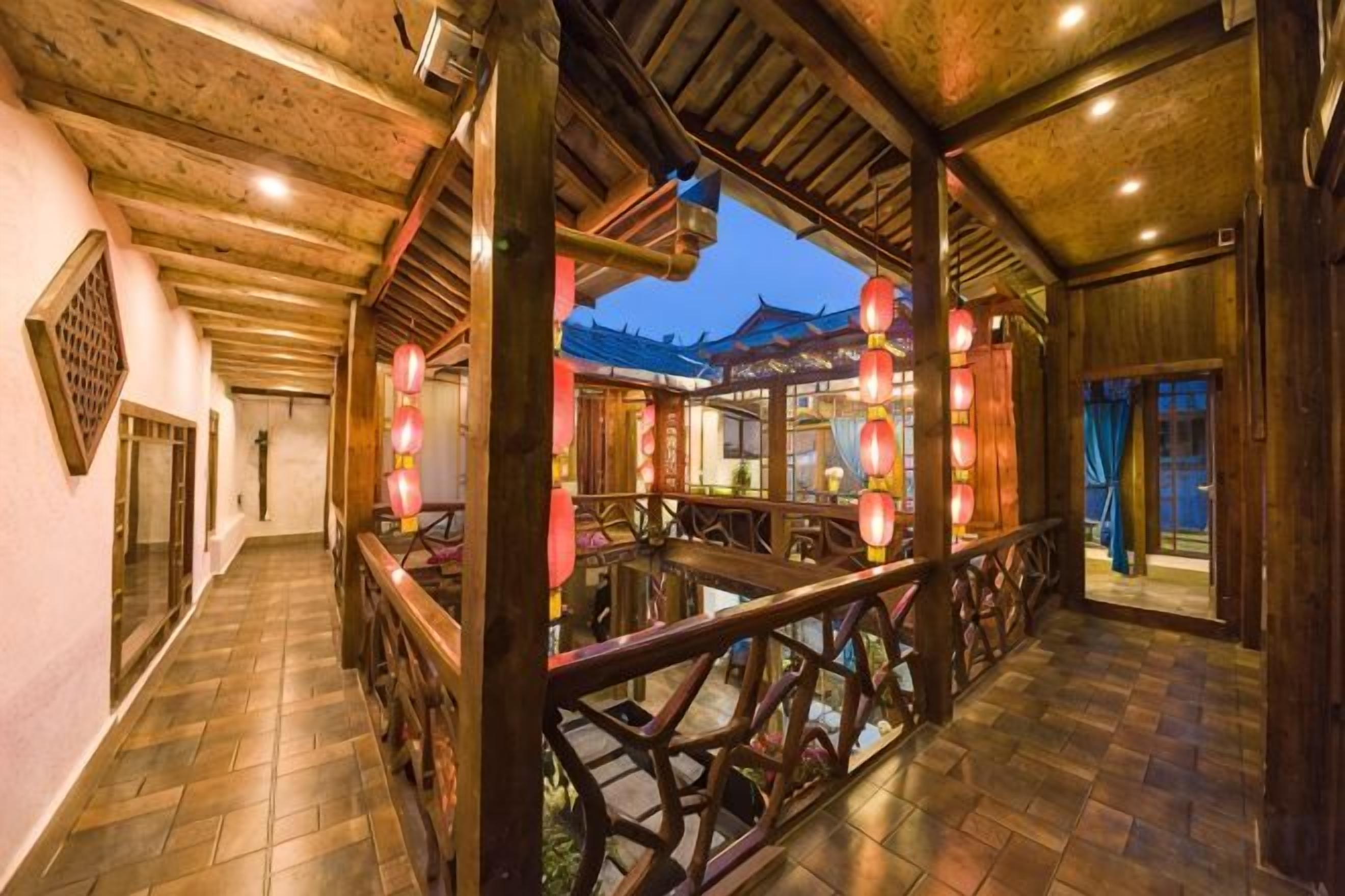 A corridor with traditional wooden architecture, a view of a restaurant with red lanterns, and a tiled floor.