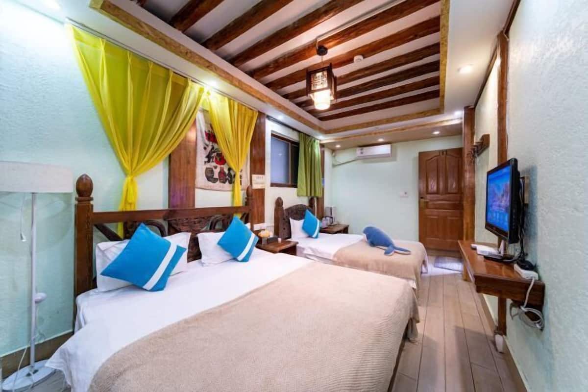 A room with two beds, a television, wooden ceiling beams, and a window with curtains.