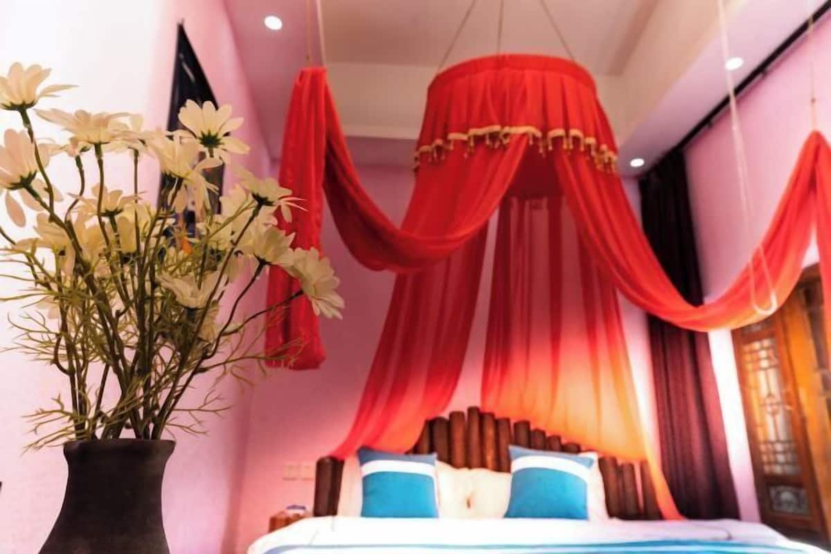 A bedroom with a bed, a vase of flowers, and red drapes.