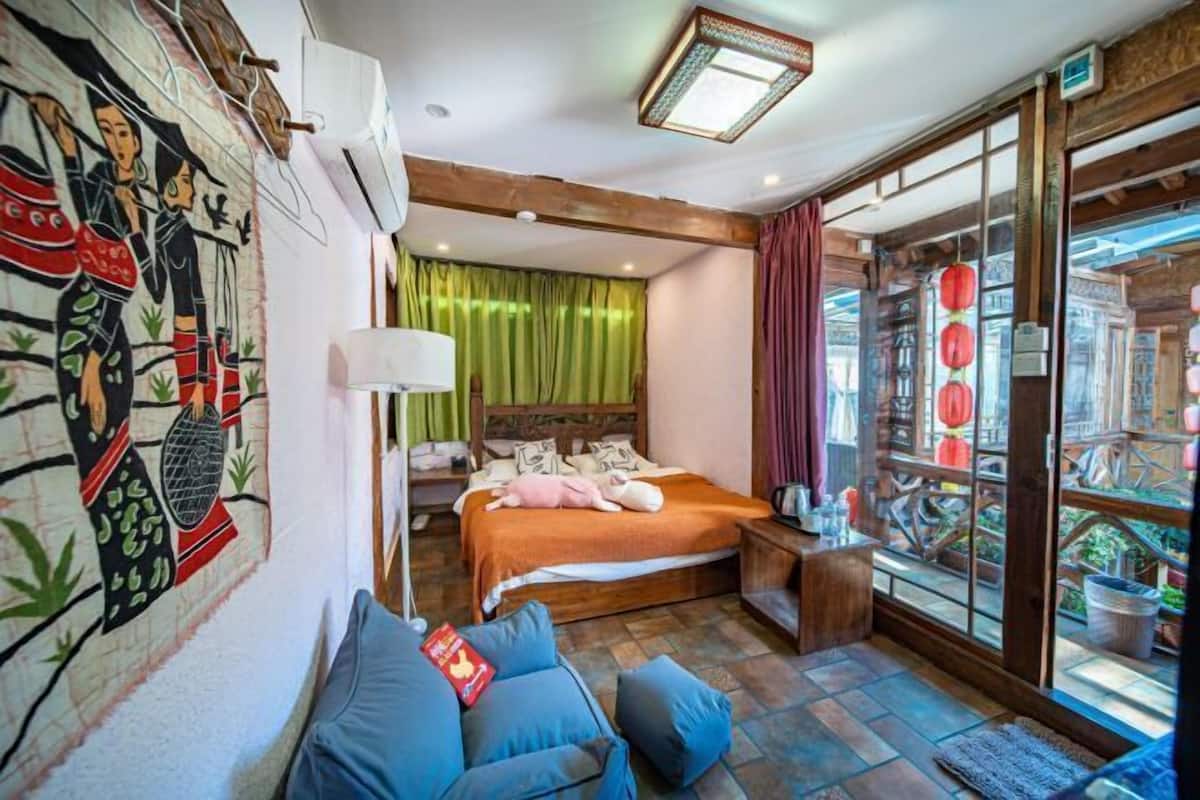 A bedroom with a bed, a nightstand, a blue sofa, a wall mural, and a large window with curtains.