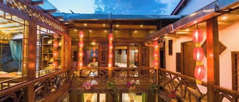A traditional wooden building with a courtyard, featuring a dining area with tables and chairs, and a visible entrance.