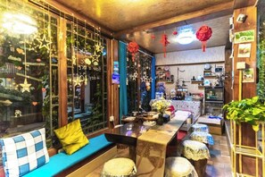 A cozy room with a wooden ceiling, a sofa with a blue cushion, a dining table with chairs, and a small kitchen area. - Lijiang Clouds flying high Inn (Lijiang)