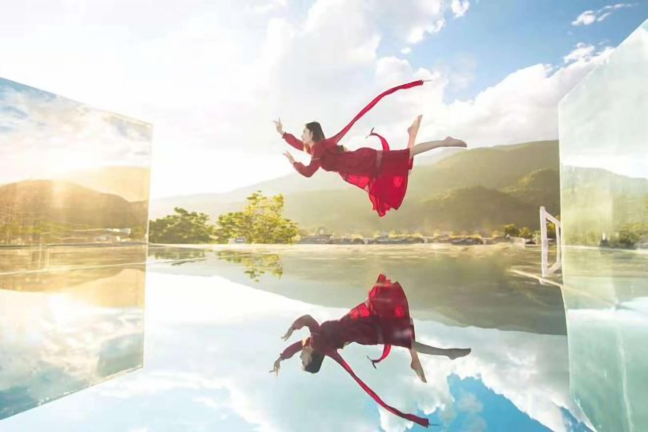 A reflection of a person in a red dress on a glass surface, with a mountainous landscape and a clear sky in the background.