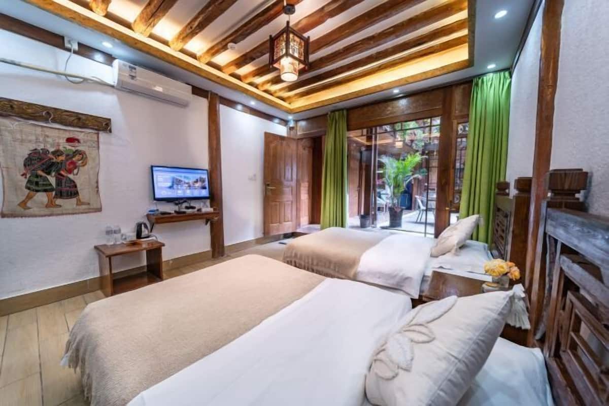 A hotel room with two beds, a television, a desk with a computer, and a window with curtains.