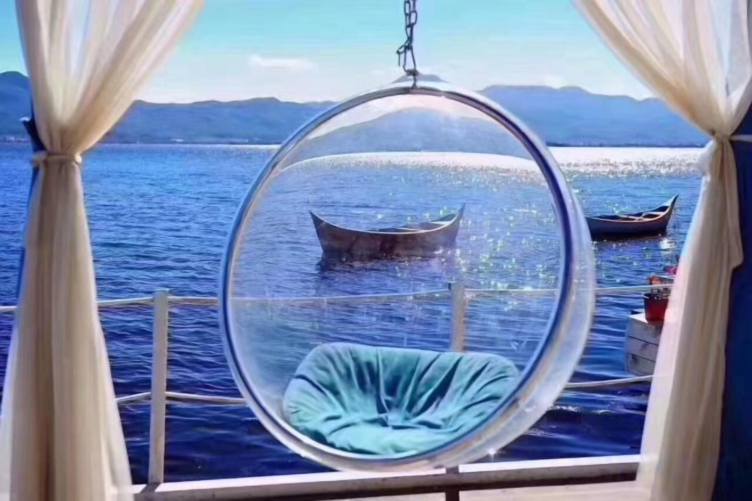 A circular hanging chair with a cushion, overlooking a body of water with boats.