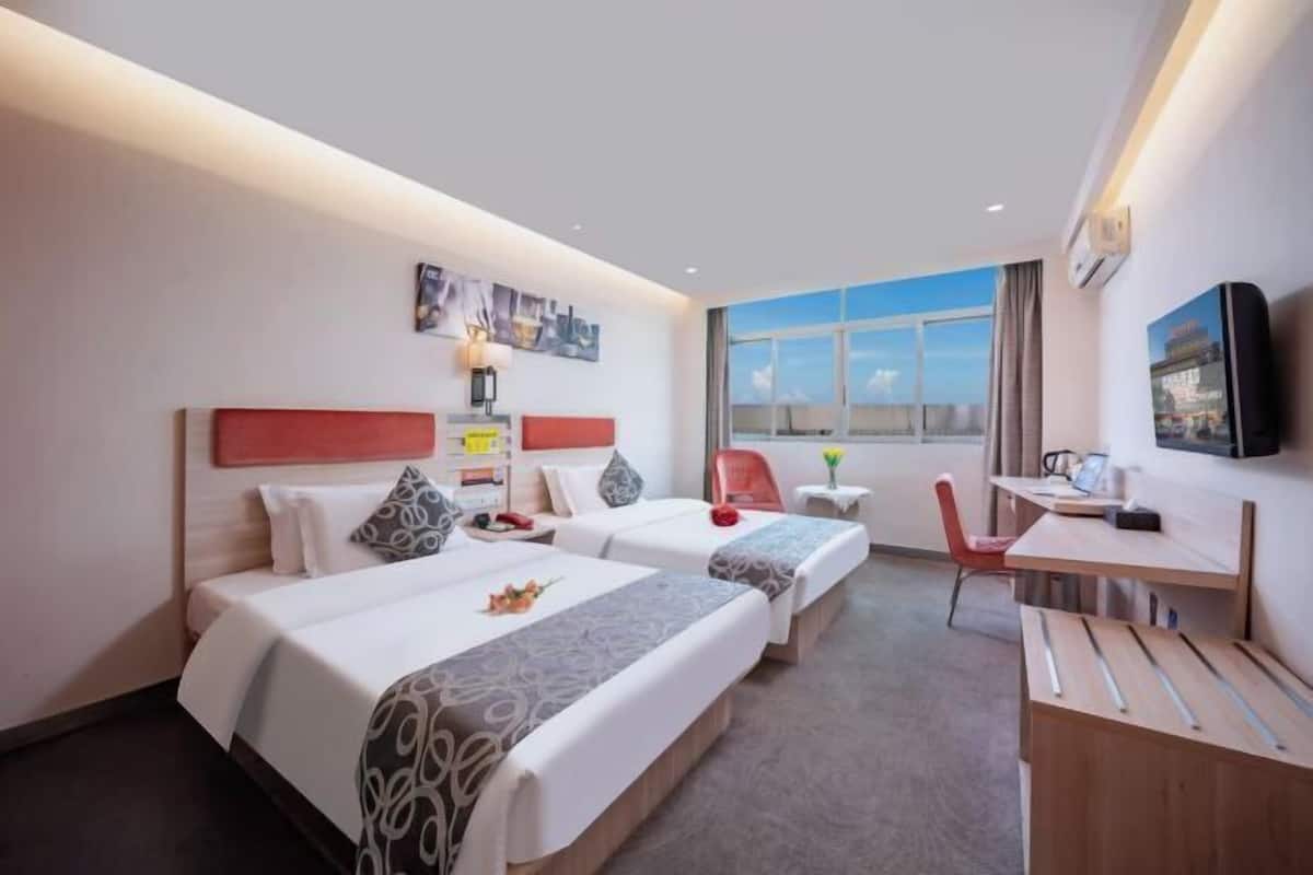 A hotel room with two beds, a desk, a chair, a TV, and a window with a view.