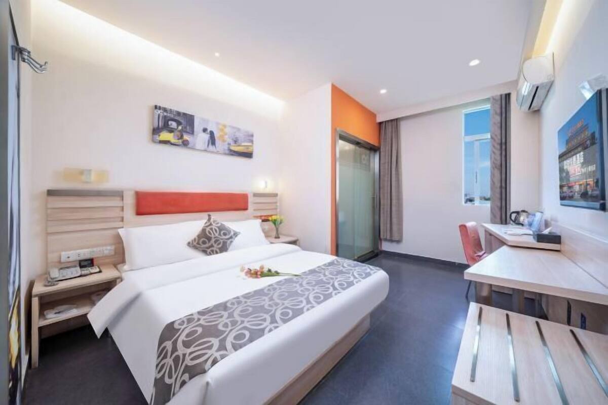 A hotel room with a bed, bedside table, nightstand, desk, chair, and a glass partition.