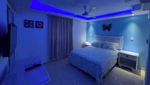 Une chambre à coucher avec un lit, des tables de chevet, un ventilateur de plafond et un téléviseur.
