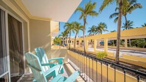 Un balcon avec des chaises turquoise, un bâtiment jaune et des palmiers en arrière-plan.