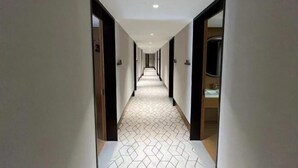 Ein Hotelkorridor mit einem gemusterten Boden, Türen auf beiden Seiten und einem Spiegel an der rechten Wand.