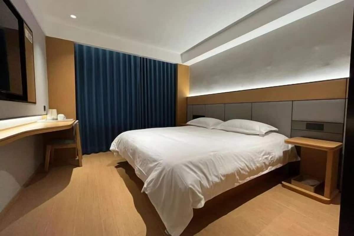 A hotel room with a bed, a desk, a chair, a bedside table, and a large mirror.