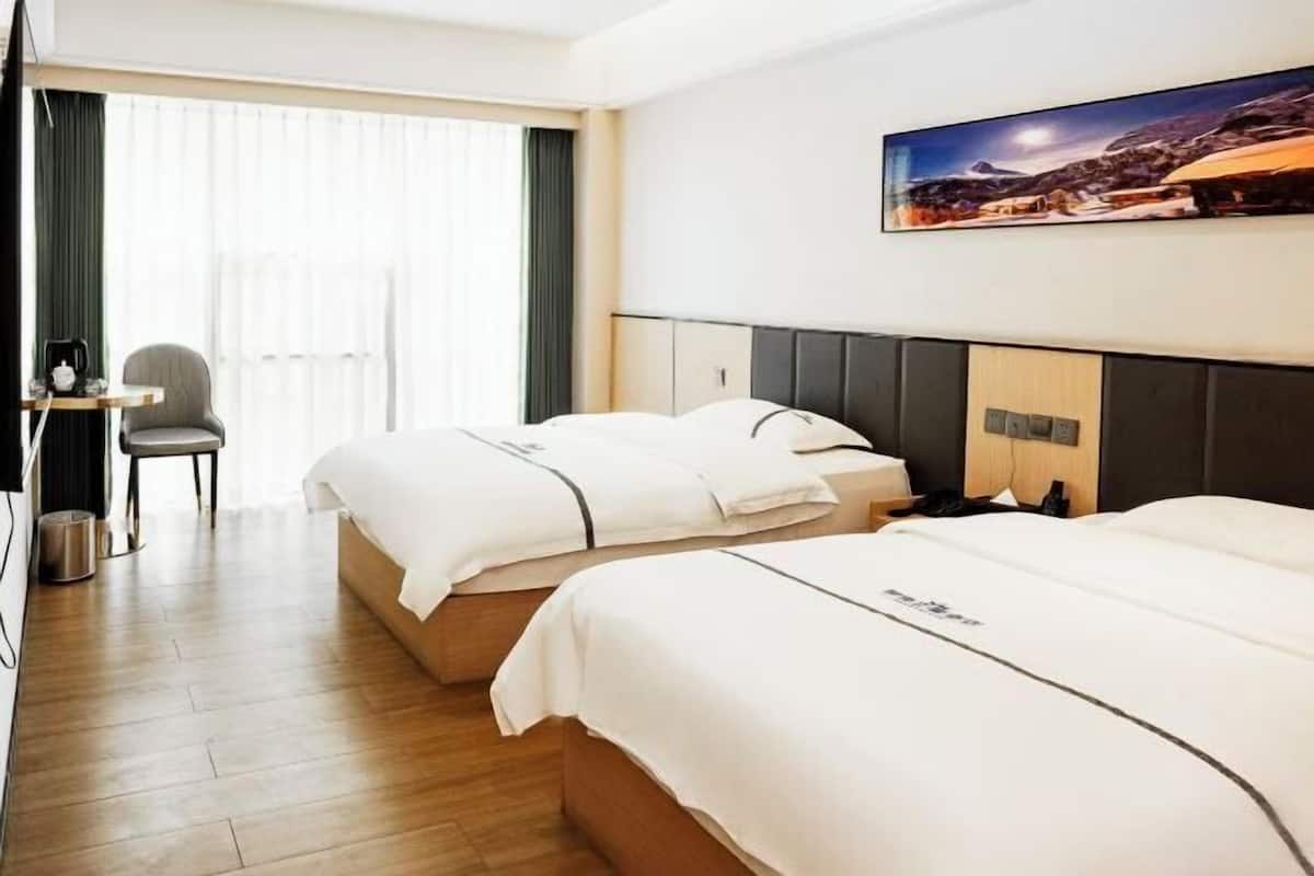 A hotel room with two beds, a desk, a chair, a painting on the wall, and a window with curtains.