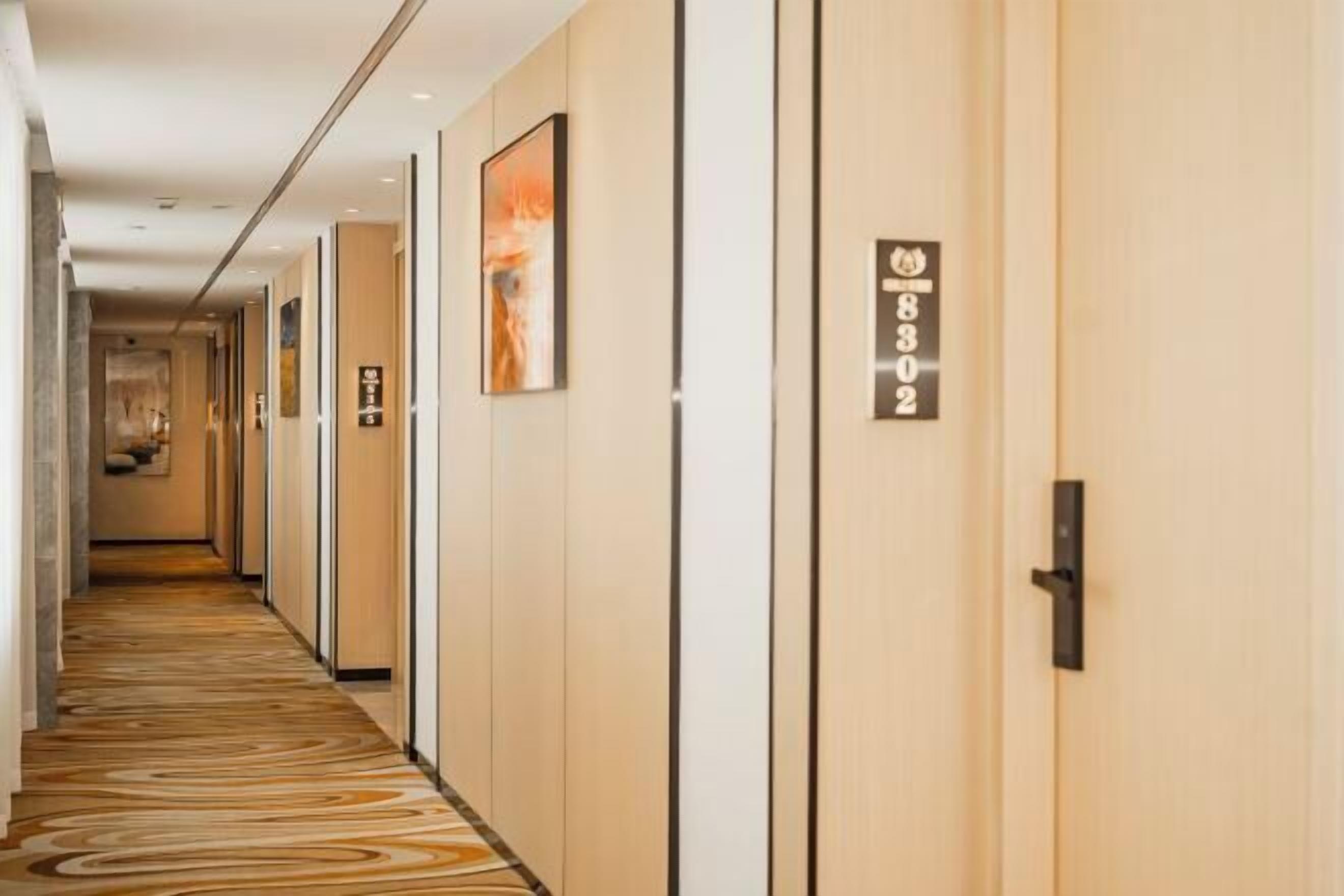 A hotel corridor with wooden doors, numbered room signs, and framed artwork on the walls.