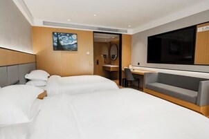 Habitación de hotel con dos camas, un escritorio, un sofá, un televisor y un cuadro en la pared.