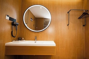 A bathroom with a wooden wall, a round mirror, a white sink, and a hairdryer. - Pink Memory Hotel (Jinshan Plaza Changjiang Road Underground Commercial Street) (Tongling)