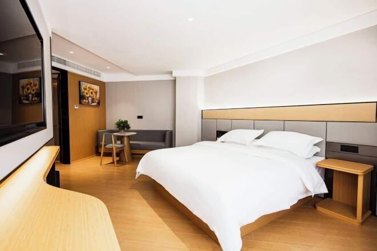 A modern hotel room with a large bed, a small desk, a chair, a TV, and a plant.