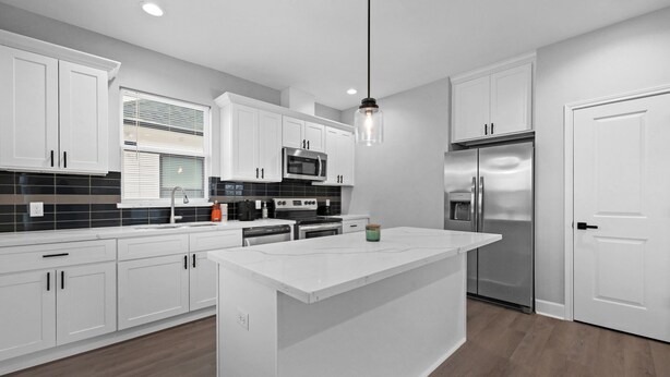 A modern kitchen with white cabinetry, a central island, stainless steel appliances, and a pendant light.