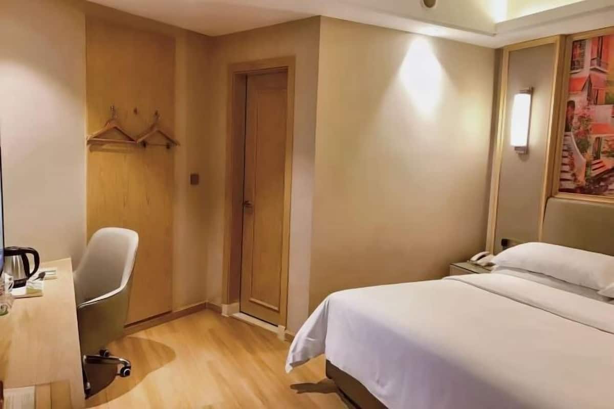 Una habitación de hotel con cama, escritorio con silla, perchero y puerta.