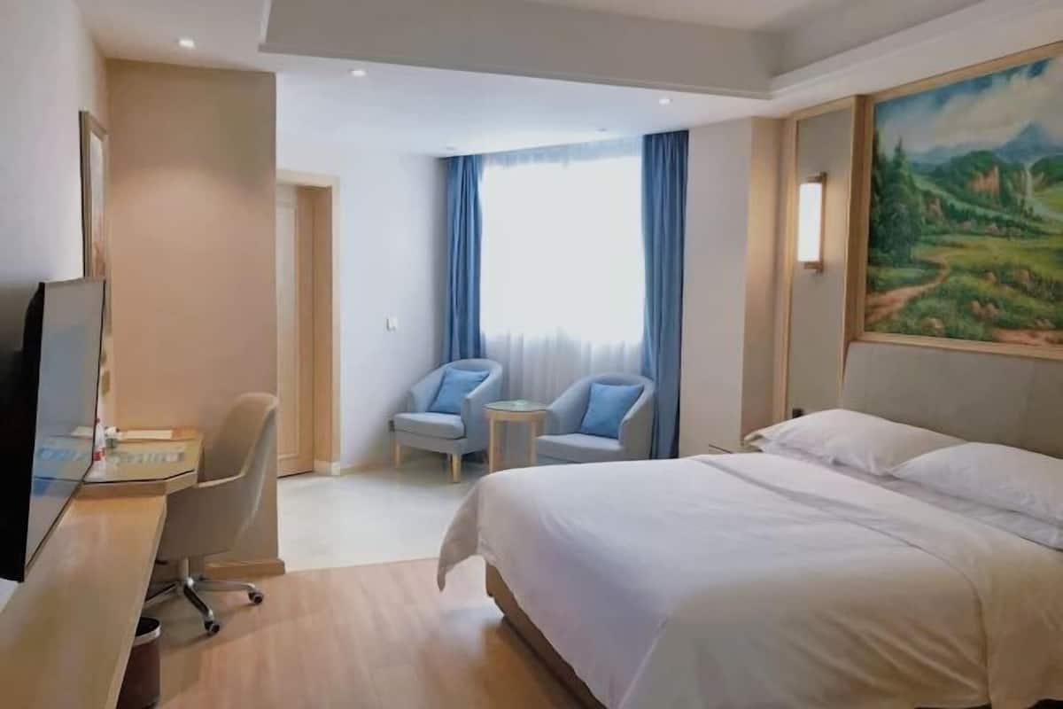 Habitación de hotel con cama, escritorio con computadora, dos sillas, una mesita y un cuadro en la pared.