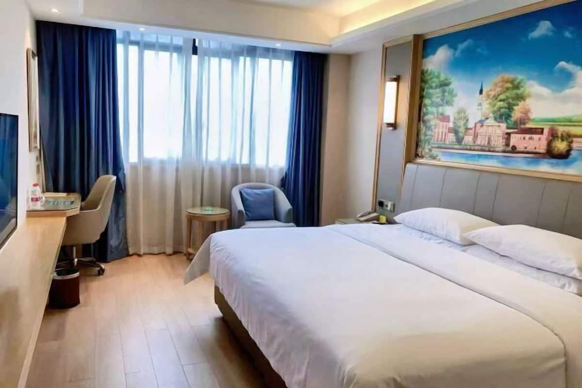 Una habitación de hotel con cama, escritorio, silla, una mesita y un cuadro en la pared.