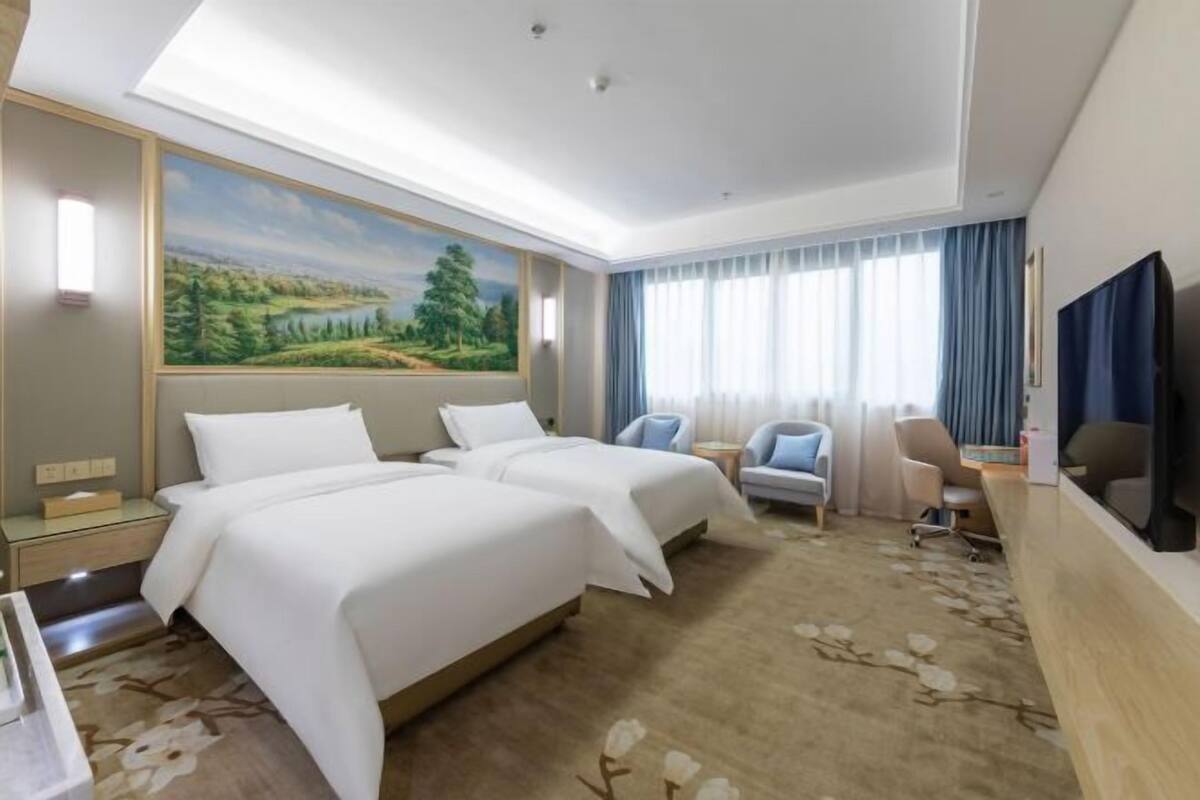 Habitación de hotel con dos camas, un escritorio, una silla, un televisor y un ventanal con cortinas.