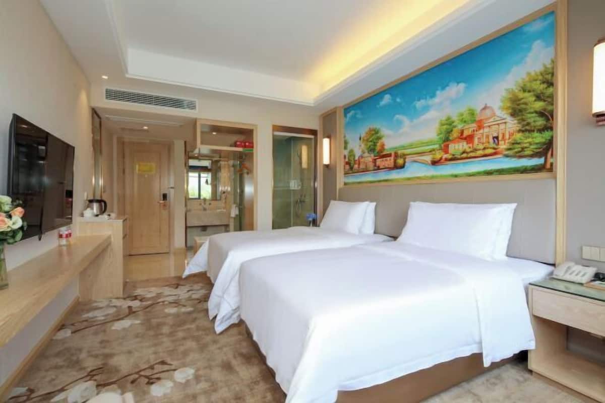 Habitación de hotel con dos camas, un cuadro en la pared, televisión y escritorio con teléfono.