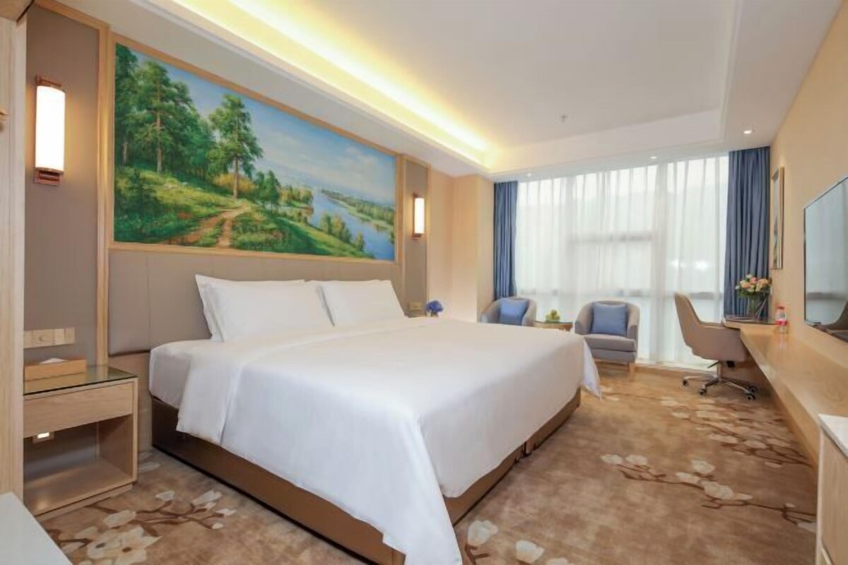 Ein Hotelzimmer mit einem großen Bett, einem Schreibtisch, einem Stuhl und einem Gemälde an der Wand.